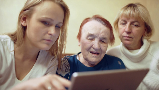 年轻女性和她的母亲还有年迈的祖母一起看平板电脑显示的照片视频