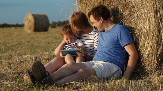 年轻的夫妇和儿子一起坐在田里干草堆上享受快乐时光视频