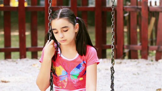 悲伤的年轻女孩坐在夏天公园的秋千上视频
