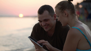 日落时海滩上的夫妇看着ipad上的照片说笑23秒视频