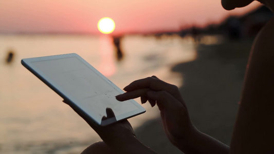 女孩使用平板电脑坐在日落海滩特写镜头视频