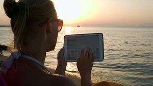 日落时女人坐在海滩上使用平板回复邮件15秒视频