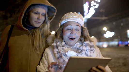 寒冷的夜晚一母女在街上边走边看平板电脑视频