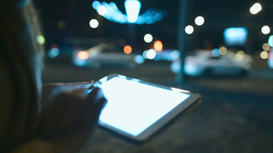 夜晚一名妇女在街上散步同时在平板电脑上打字聊天视频