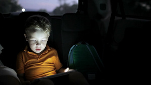 小男孩晚上在车后座用触控板玩游戏16秒视频