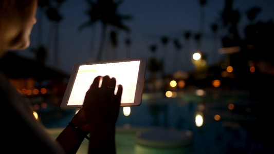 夜晚美丽的热带度假村正在使用平板电脑的女人视频