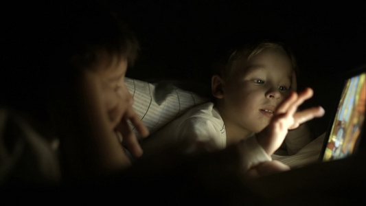 两个男孩躺在床上玩平板电脑视频