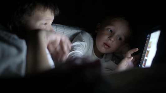夜晚两个小朋友躲在被窝玩平板电脑视频
