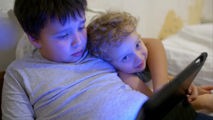 两个小男孩躺在床上玩平板电脑里的游戏16秒视频