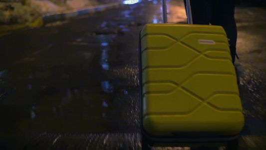 孤独的女人夜晚拉着黄色行李箱走在潮湿的人行道上视频