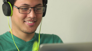 亚洲男人在沙发上用平板电脑上看视频戴着绿色的大耳机听音乐10秒视频