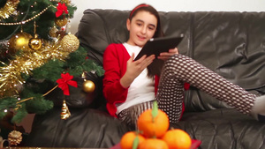 女孩坐在圣诞树旁边的沙发上玩她的平板电脑28秒视频