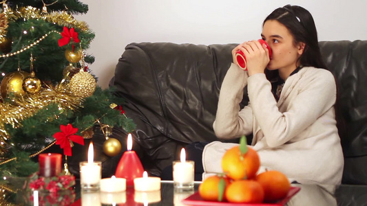 女孩坐在圣诞树旁的沙发上喝热水视频