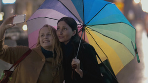 雨天打着五彩雨伞的年轻女子和她的母亲在街上自拍25秒视频