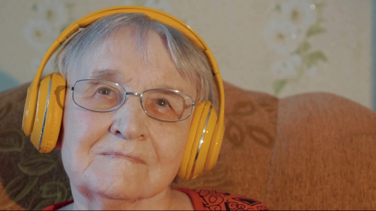 戴着耳机的白发女人坐在沙发上听音乐视频