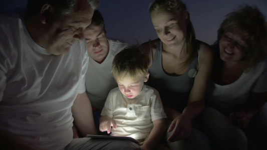 夜晚小男孩和他的家人们在户外使用平板电脑视频