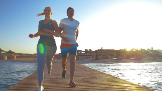 阳光下一对年轻夫妇沿着木墩跑步[依靠]视频