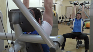 从健身房的镜子里看到一个年轻人在用压肩机做着运动19秒视频
