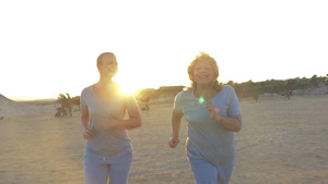 年轻的女人和母亲在海边夕阳的落日下奔跑20秒视频