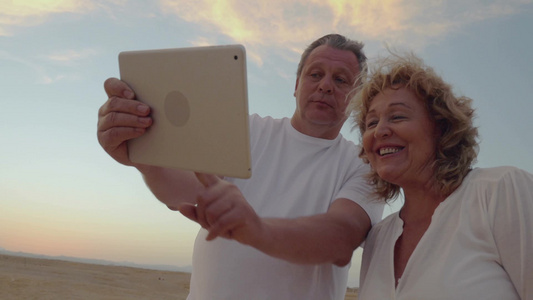 夕阳下快乐的老年夫妇用平板电脑在自拍视频