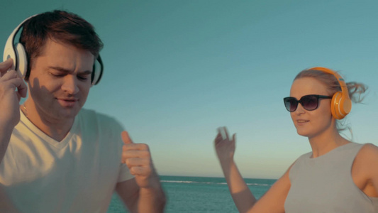 年轻男人和女人在海滩上戴着无线耳机唱歌跳舞[二十多岁]视频