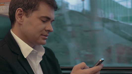火车上的白领男人在智能手机上发短信视频