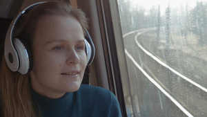 年轻的女人戴着无线耳机在火车上随着音乐放松同时欣赏着窗外美丽的风景29秒视频