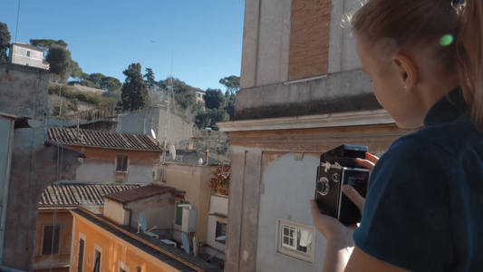 女人站在阳台上用复古相机拍摄城市景观视频