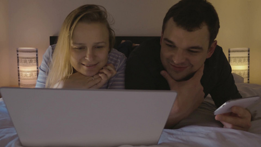 年轻夫妇躺在床上看笔记本电脑视频