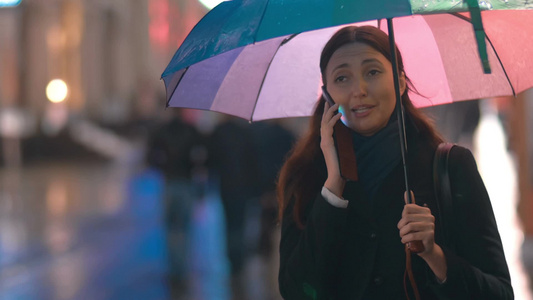 女人在城市的雨夜里拿着雨伞令人兴奋的电话交谈视频