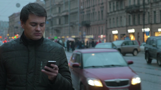 雨夜一个年轻人站在繁忙的城市道路旁发短信视频