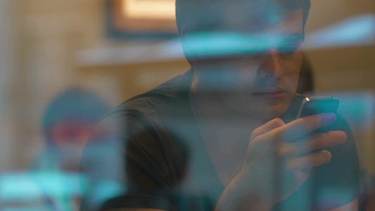 年轻人坐在咖啡馆里玩手机透过窗户看人们走在外面反射玻璃视频