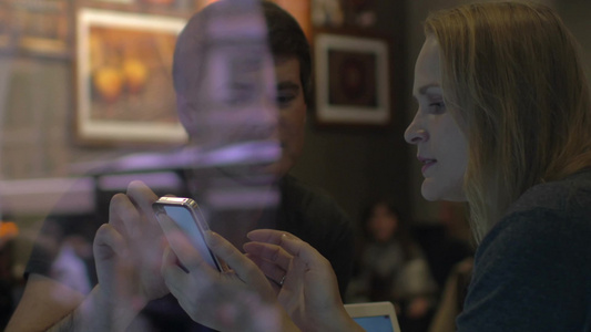 年轻男女坐在咖啡馆看着智能手机谈论视频