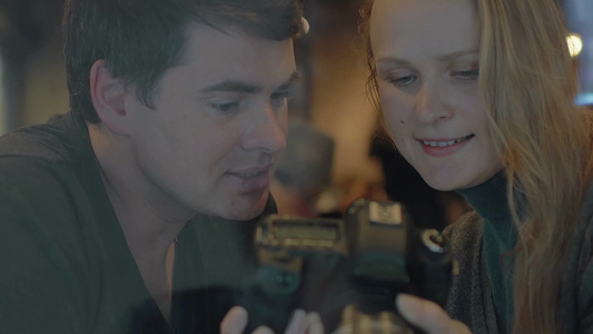 年轻夫妇在咖啡馆里用数码相机看照片视频