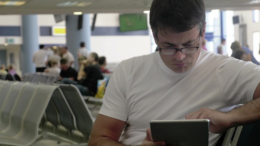年轻男人在机场候车室里使用数字平板电脑办公视频