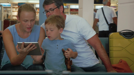父母和小儿子在机场的候机室使用平板电脑视频