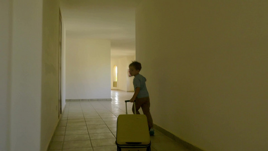 一个小男孩拉着他的行李箱沿着酒店走廊跑着视频