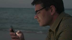 夜晚戴着眼镜的中年男人在海滩上用智能手机发短信聊天13秒视频