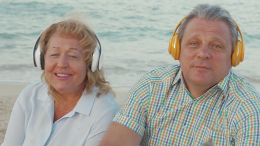 老年夫妇在海边戴着无线耳机听音乐视频