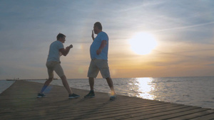 在日落时年轻的儿子和他的父亲站在海岸的木桥上玩拳击游戏23秒视频