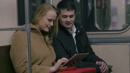 年轻夫妇坐在地铁里用平板电脑打发时间视频