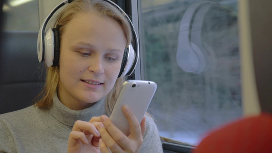 乘火车旅行年轻的女人正在听耳机里的音乐同时在智能手机上写信息视频