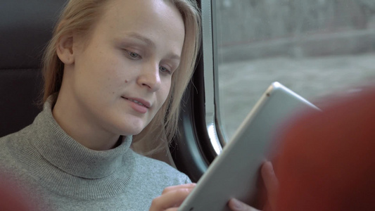 年轻的女人坐在靠窗的火车车厢里使用平板电脑上打字视频