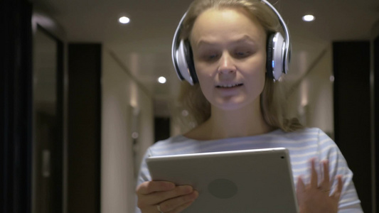 一位年轻女子戴着耳机里拿着平板电脑浏览网页视频