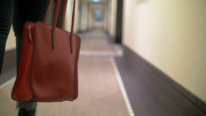 一个年轻女人沿着走廊走着手里拿着一个红色皮包的特写33秒视频