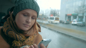 年轻女人在乘坐公共汽车时使用智能手机看着潮湿的窗户25秒视频