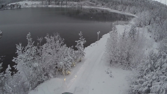 驾驶汽车沿着雪路在湖边穿过松树和冰冻的树木行驶到冬令营视频