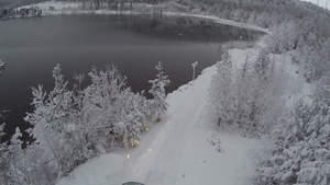 驾驶汽车沿着雪路在湖边穿过松树和冰冻的树木行驶到冬令营39秒视频