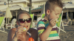 戴太阳镜的妈妈和小儿子一起在海滩上吹泡泡16秒视频