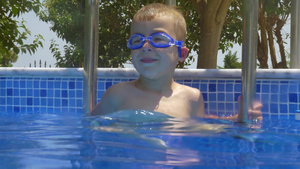 戴护目镜的小男孩在游泳池的梯子上微笑9秒视频